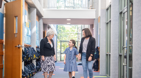 A teacher, child and mother walking around the school halls talking.