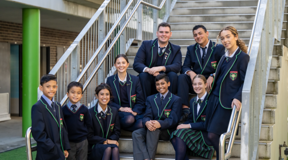 A group of high school students sitting on the steps at their Catholic school.