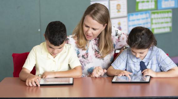 A teacher helping two students with their work on ipads.