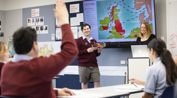 A teacher at the front of the classroom with a student. The student is presenting to the rest of the class.