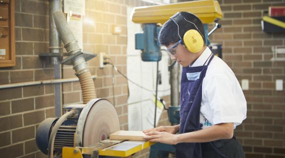 A young boy sanding wood on the circular sander.