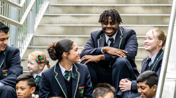 High school students sitting on the school steps smiling and laughing.