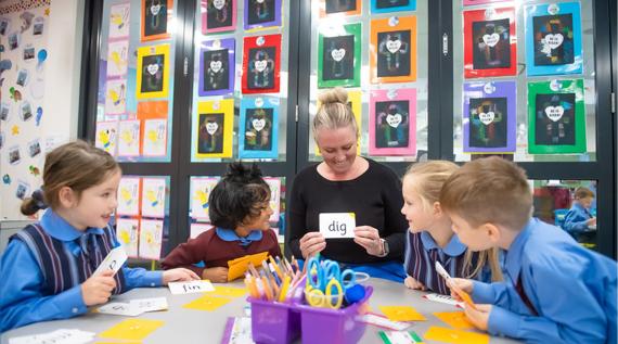 A teacher with young students. She is teaching them how to read words.