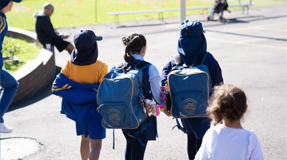 Kids walking into school with their school bags on.