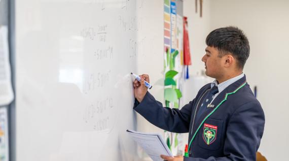 A high school student doing some complex mathematics on a white board.