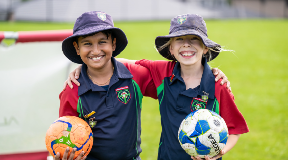 Two students holding sports balls smiling on the sports field.