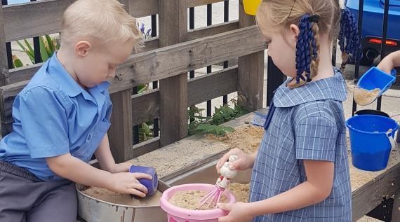 Two young children playing in a sand pit with buckets and spades.