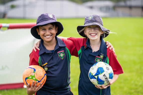 Two students holding sports balls smiling on the sports field.