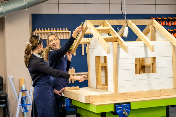 Two students building a dog house in woodwork.