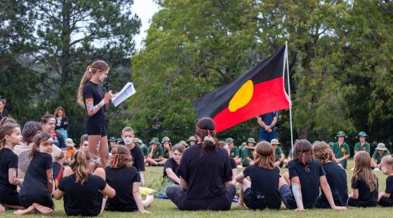 An Aboriginal flag inside a circle of students who are wearing cultural Aboriginal attire.