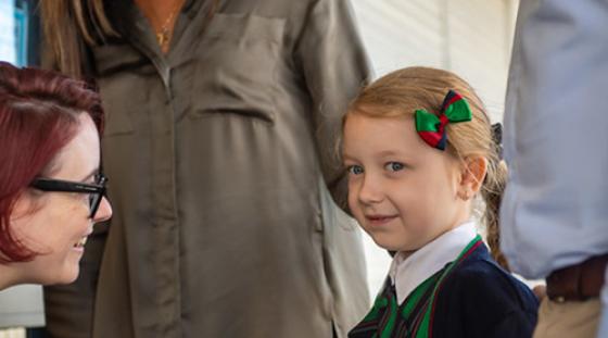 A child being welcomed to school by the teacher. She is with her parents.