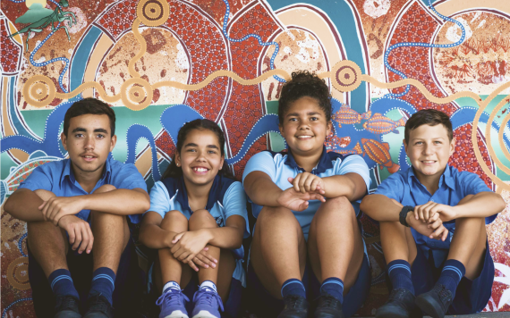 A group of Aboriginal boys in their school uniforms sitting in front of Aboriginal artwork.