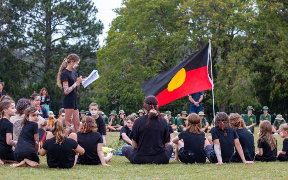 An Aboriginal flag inside a circle of students who are wearing cultural Aboriginal attire.