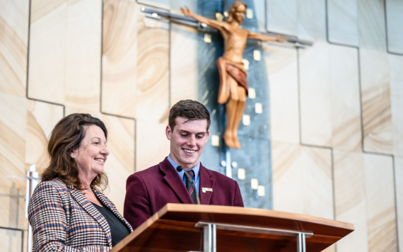 A student and a teacher standing in front of a lectern in a church.