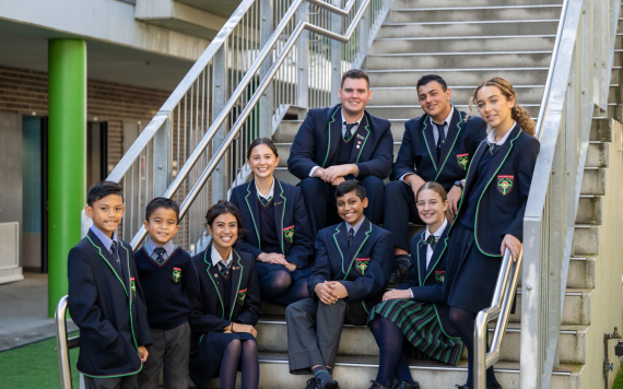 A group of high school students sitting on the steps at their Catholic school.