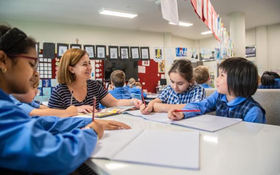 A teacher at a table with some students teaching them writing.