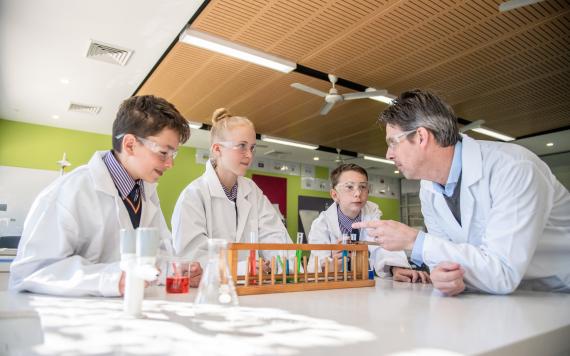 A teacher in science class showing the kids how to safely handle the test tubes with liquid in them.