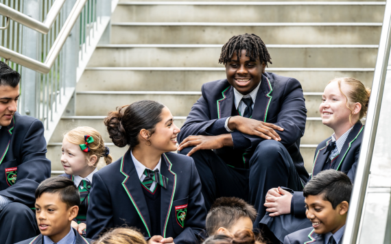 High school students sitting on the school steps smiling and laughing.