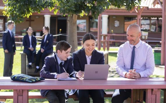 A teacher with two students in the garden area looking at a laptop together.